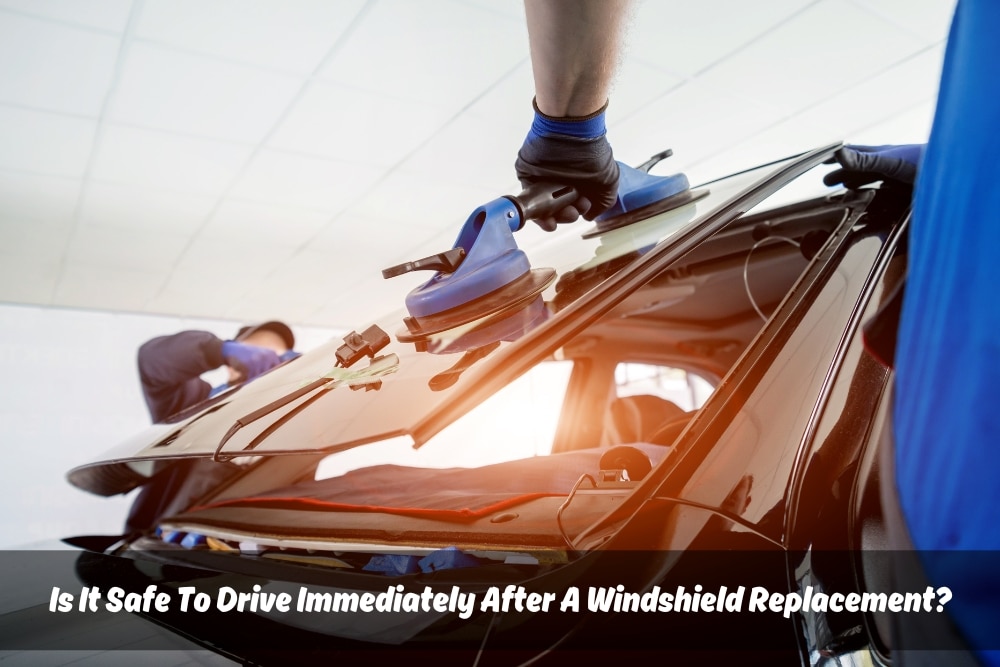 Technicians are installing a new windshield on a car using suction cups in a professional garage setting. The image illustrates the process involved in windshield replacement, highlighting the importance of proper installation before you "drive after windshield replacement" for safety.
