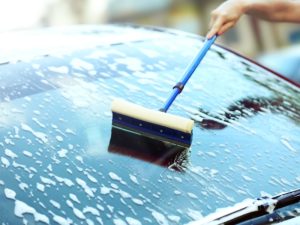 Image of a person using a sponge squeegee to clean a soapy car windscreen, showing how to clean a car windscreen.