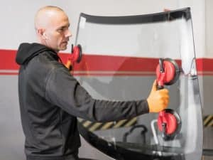 Technician replacing a leaking windscreen with specialised tools for secure installation.