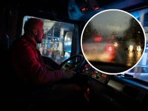 Truck driver driving in heavy rain with a leaking windscreen causing visibility issues.