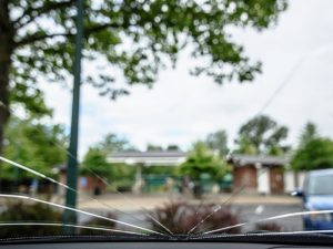 A close-up shot of a windscreen crack spidering across the glass, with a blurred outdoor scene visible through it.