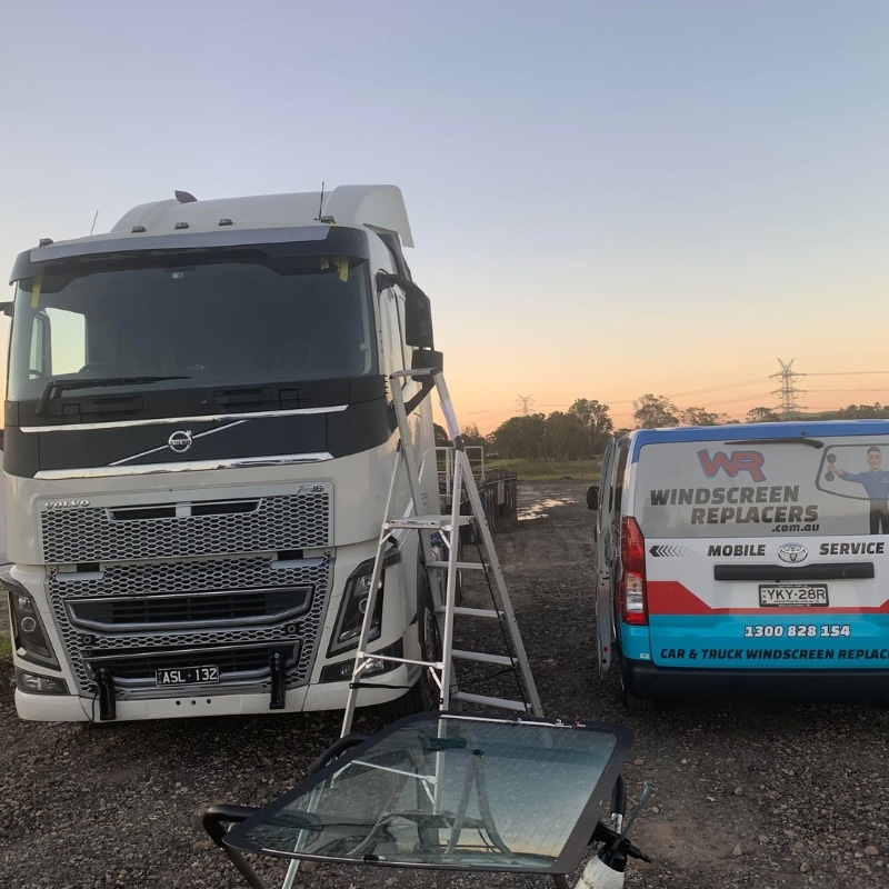 Windscreen Replacers mobile van performing truck windscreen replacement on a Volvo truck at a Sydney worksite.