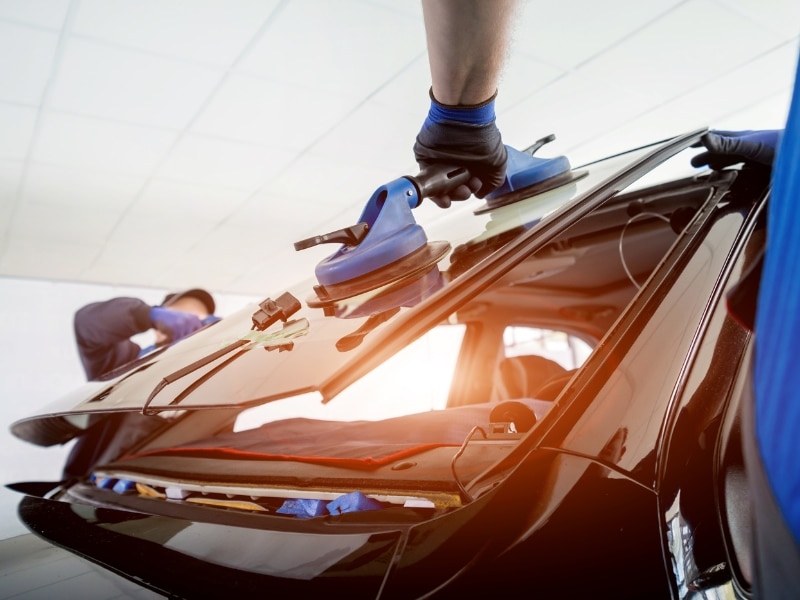Professional windscreen solutions showing technician installing new car windscreen with suction tool.